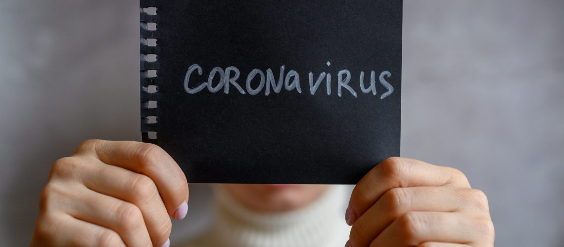 coronavirus-text-in-white-letters-on-a-black-notebook-paper-in-the-hands-of-a-woman-covers-her-face_t20_rRaYxd