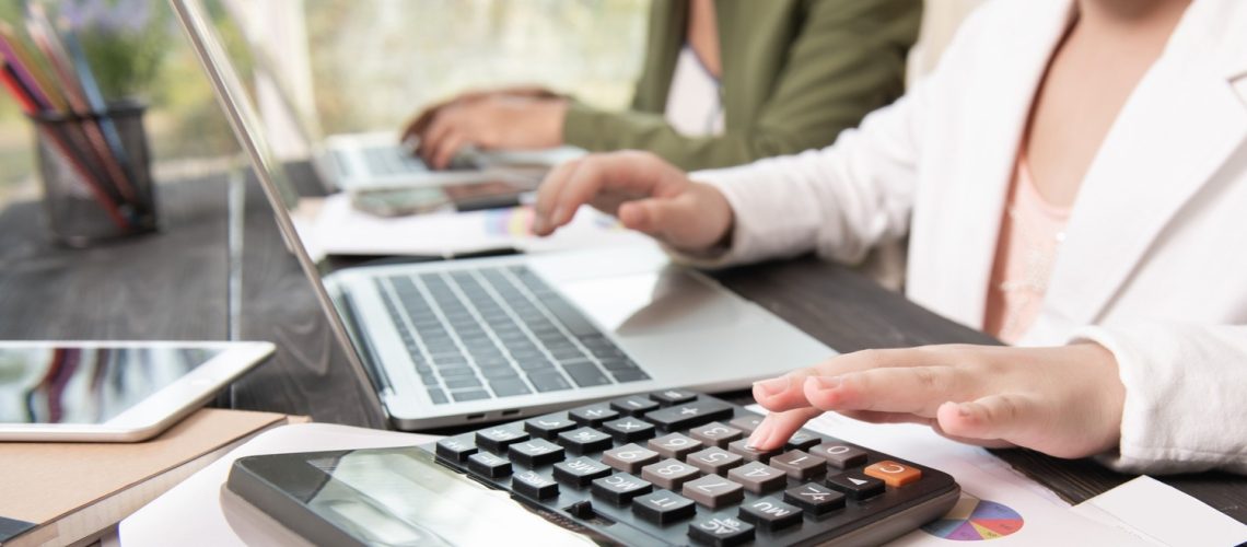 Profissionais em um escritório usando uma calculadora para calcular tributos
